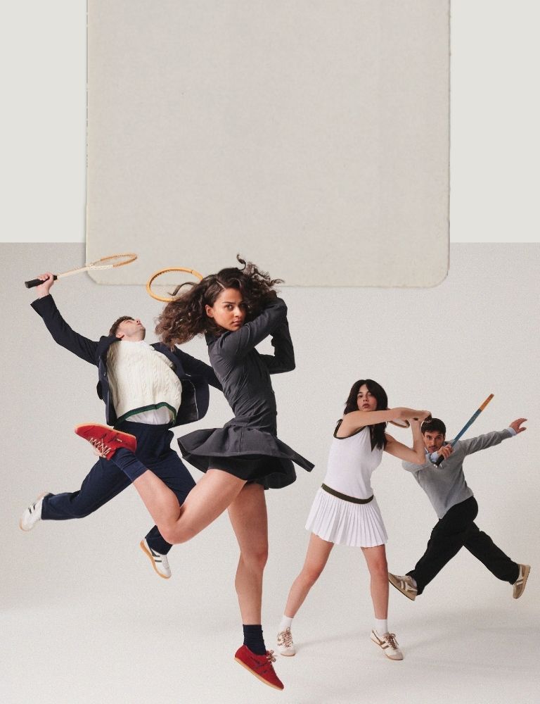 Four people in tennis attire posing with vintage wooden tennis rackets against a plain background