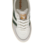 The top of a white Gola shoe with a green stripe and gold logo on the tongue.