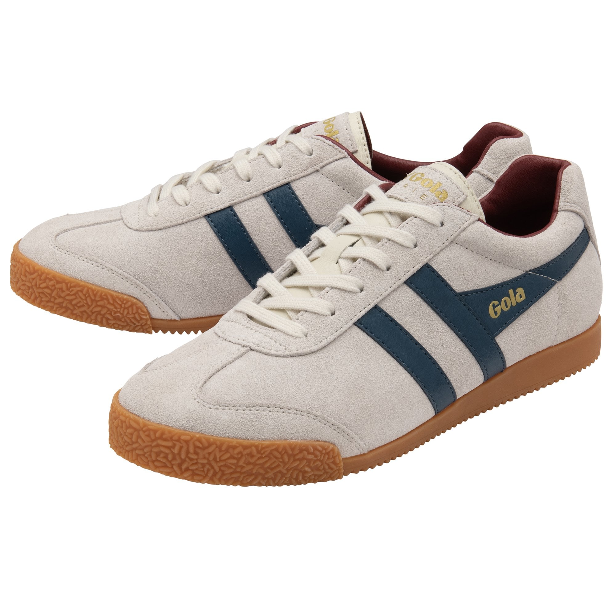 A pair of off-white Gola Harrier trainers with navy stripes and maroon lining.