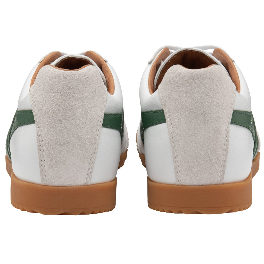 The rear view of a pair of white Gola Harrier trainers with green stripes.