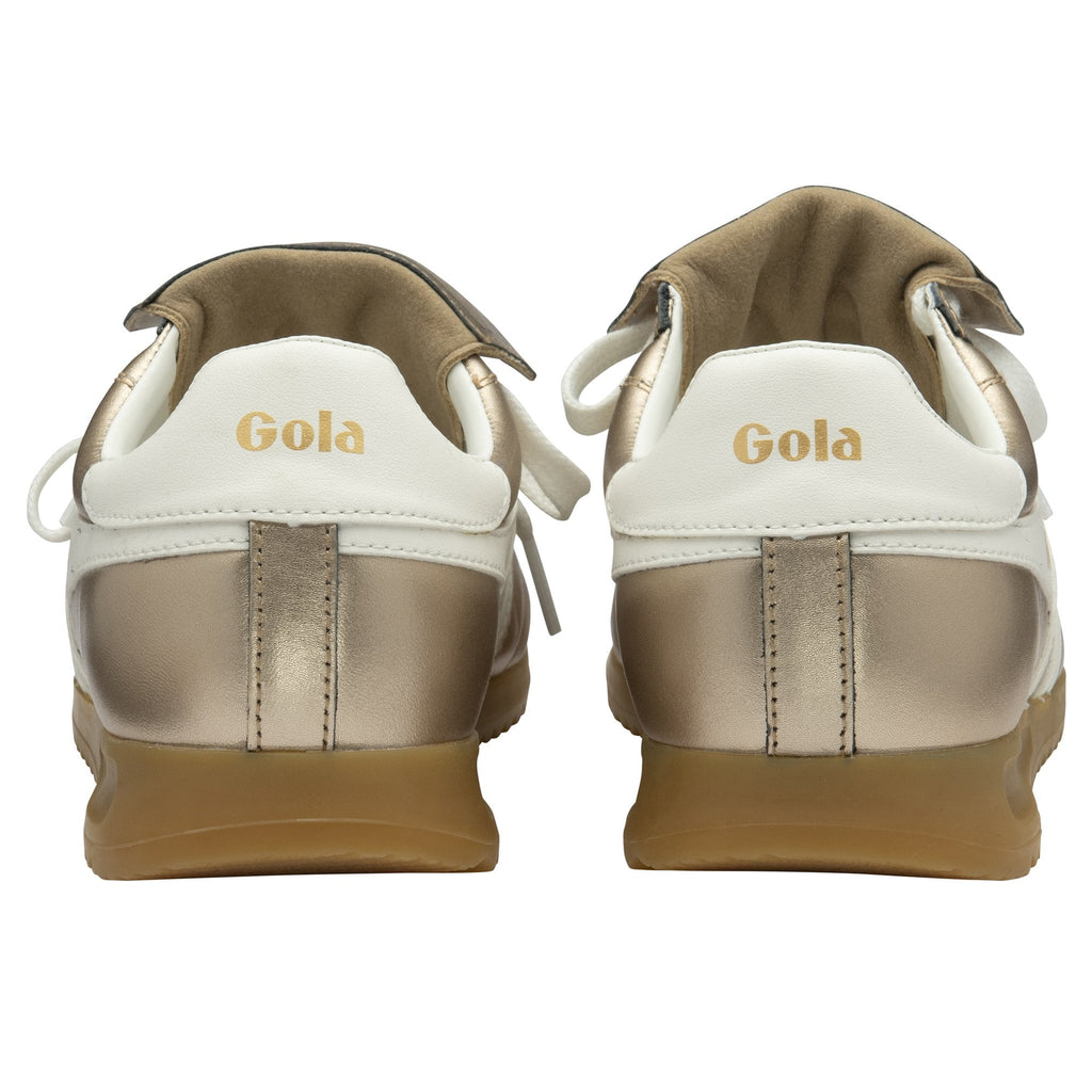 The back view of a pair of golden Gola trainers with white accents.