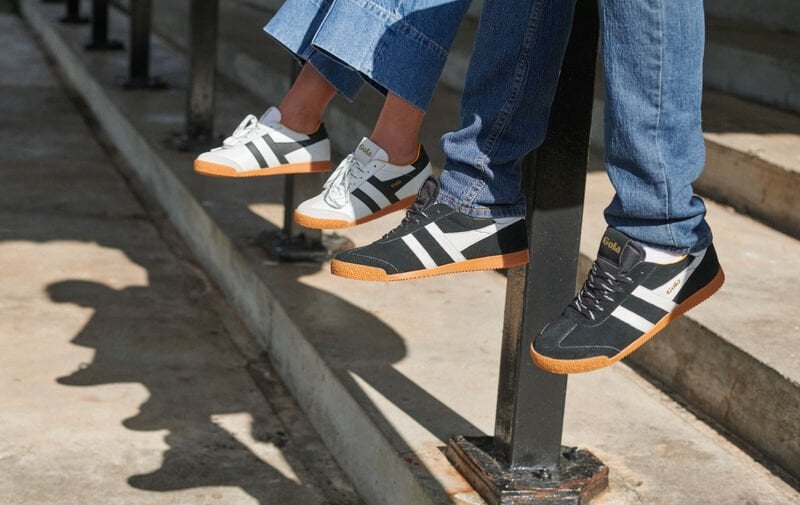 Three pairs of feet wearing black, white, and gray sneakers with gum soles, dangling over a ledge.