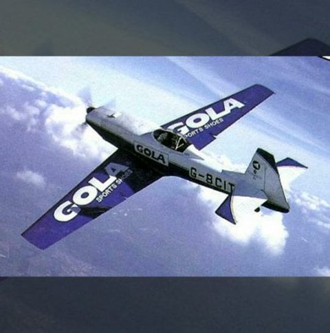 A small, silver and purple Gola-branded stunt plane flying through a cloudy sky.