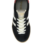 The top-down view of a black sneaker with white stripes, cream laces, and a red heel.