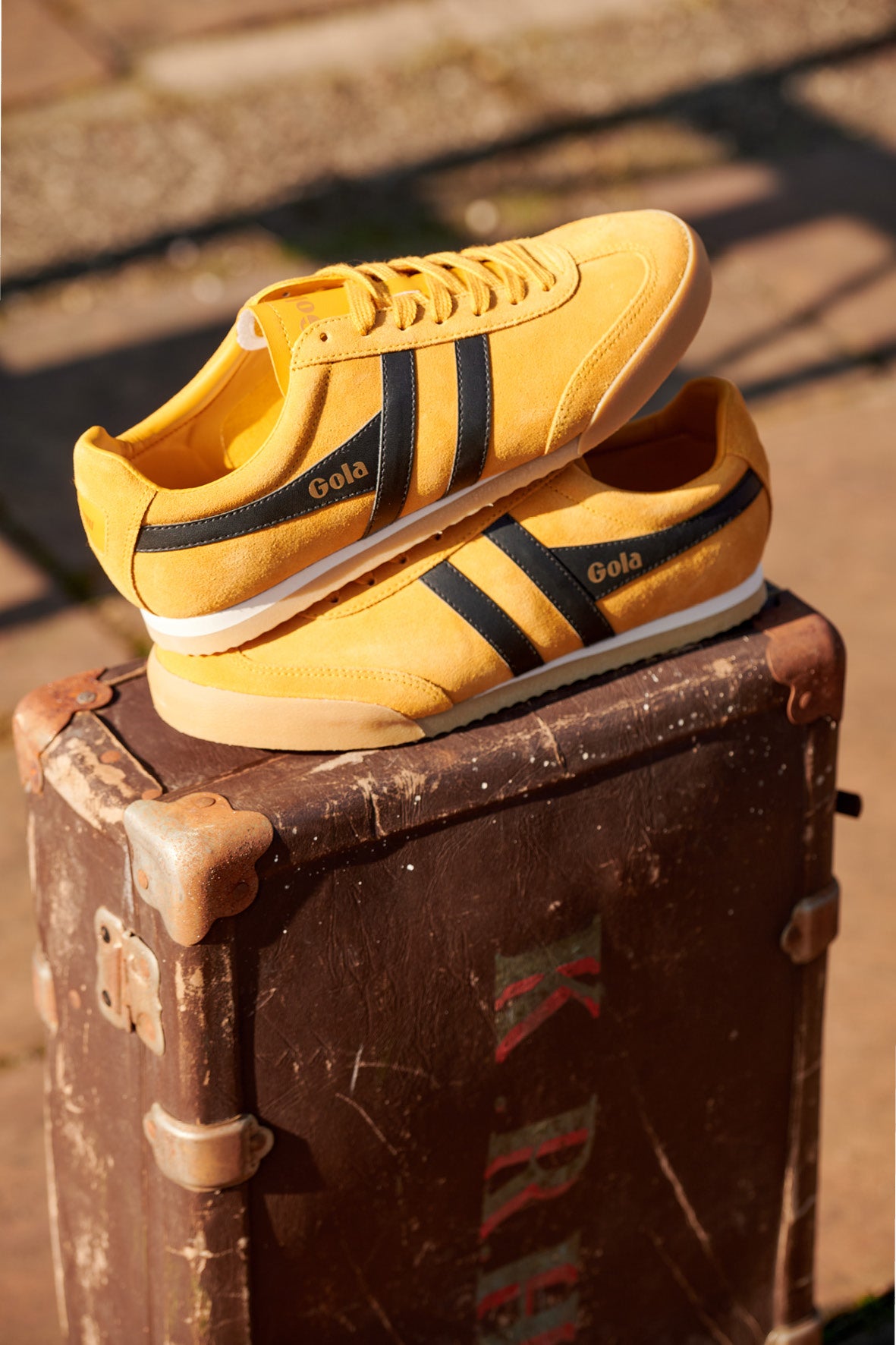 Pair of yellow Gola trainers with black stripes, stacked on a vintage brown suitcase