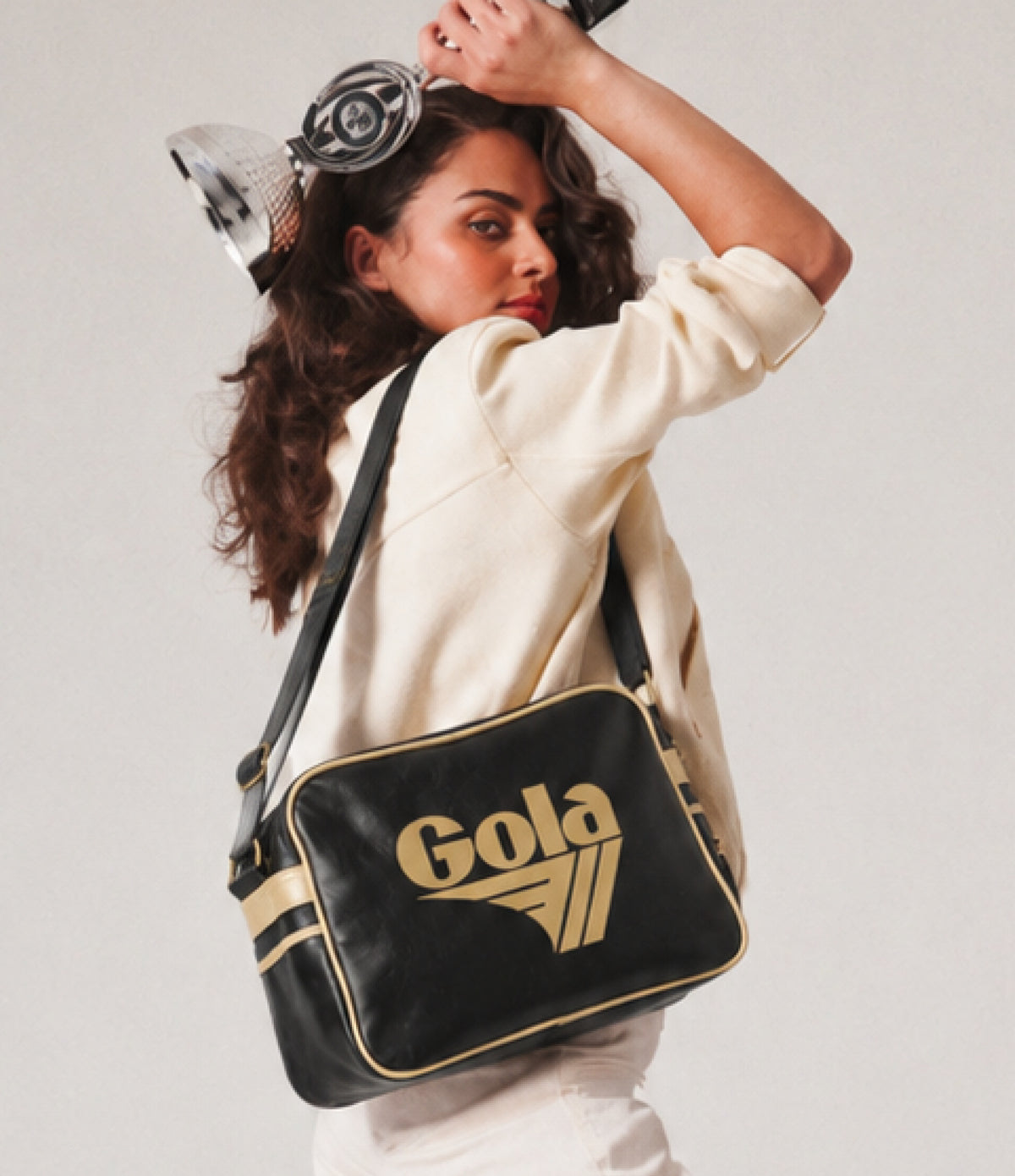 Woman wearing a black Gola shoulder bag with gold trim and logo