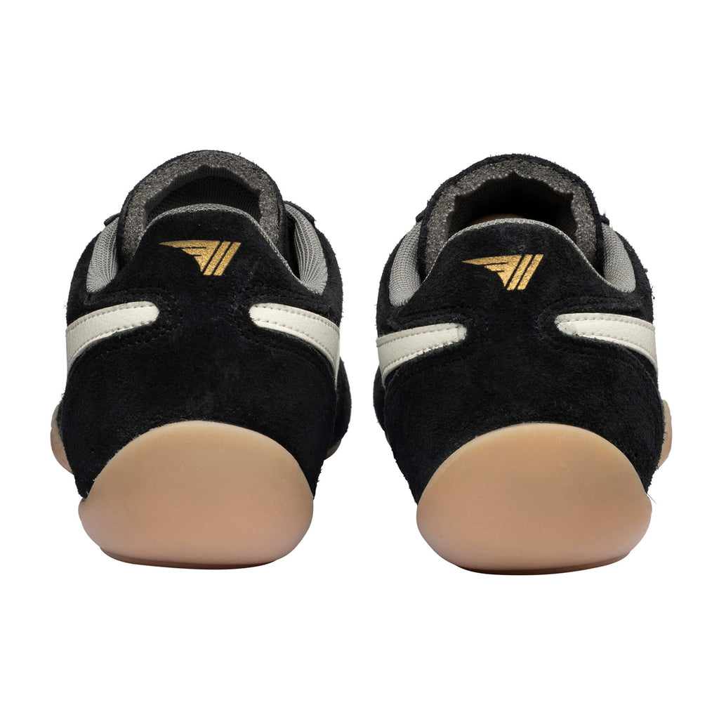 Pair of black suede trainers with white stripes and gold logo on the heel, rear view