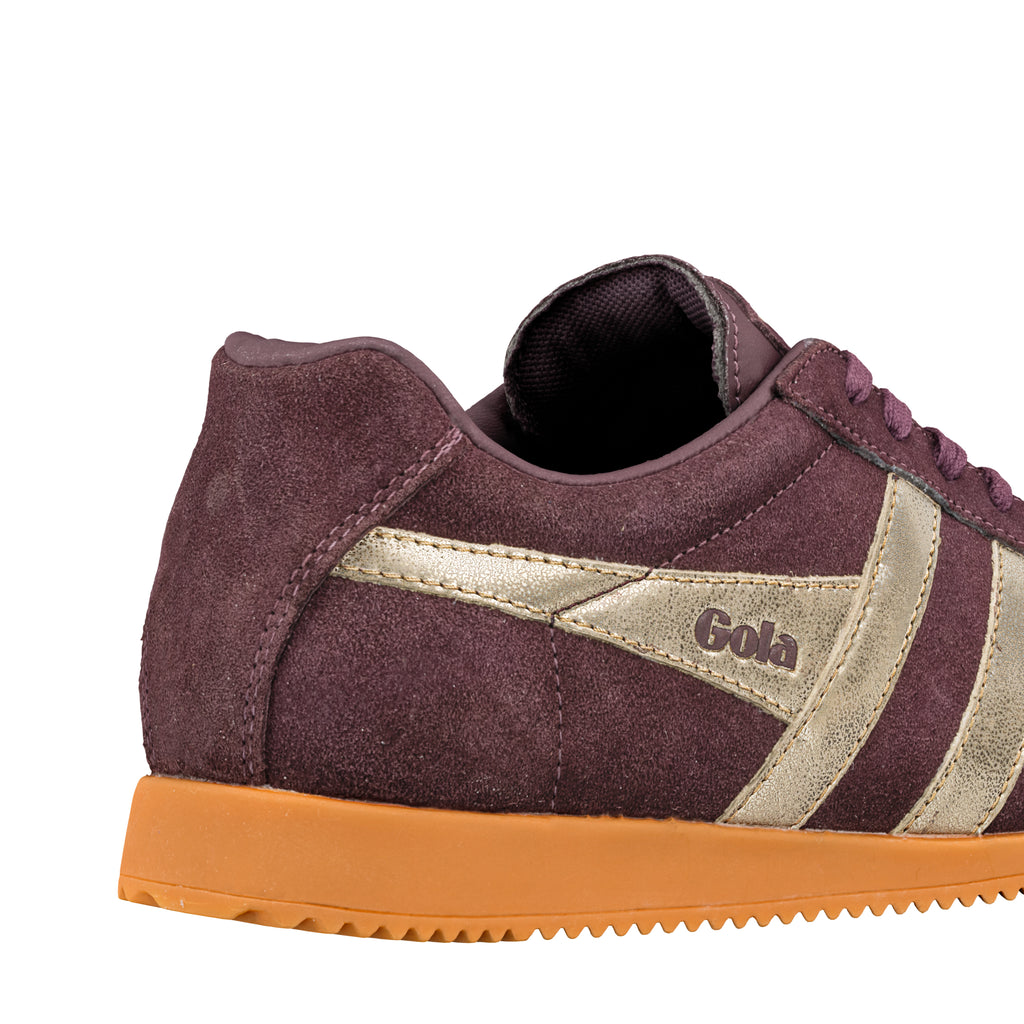 Close up of a plum suede Gola trainer with metallic gold side stripes and a gum rubber sole