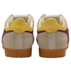 Pair of beige trainers with yellow heel tab on a white background
