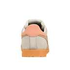 Rear view of a beige suede trainer with a peach heel tab and orange rubber sole