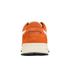 Rear view of an orange suede trainer with a cream midsole and black rubber sole