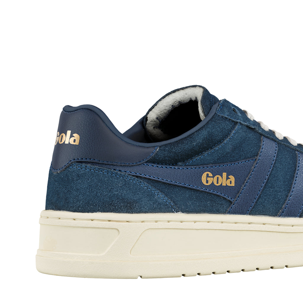 Close up of the heel and side panel of a navy blue suede and leather trainer with gold branding