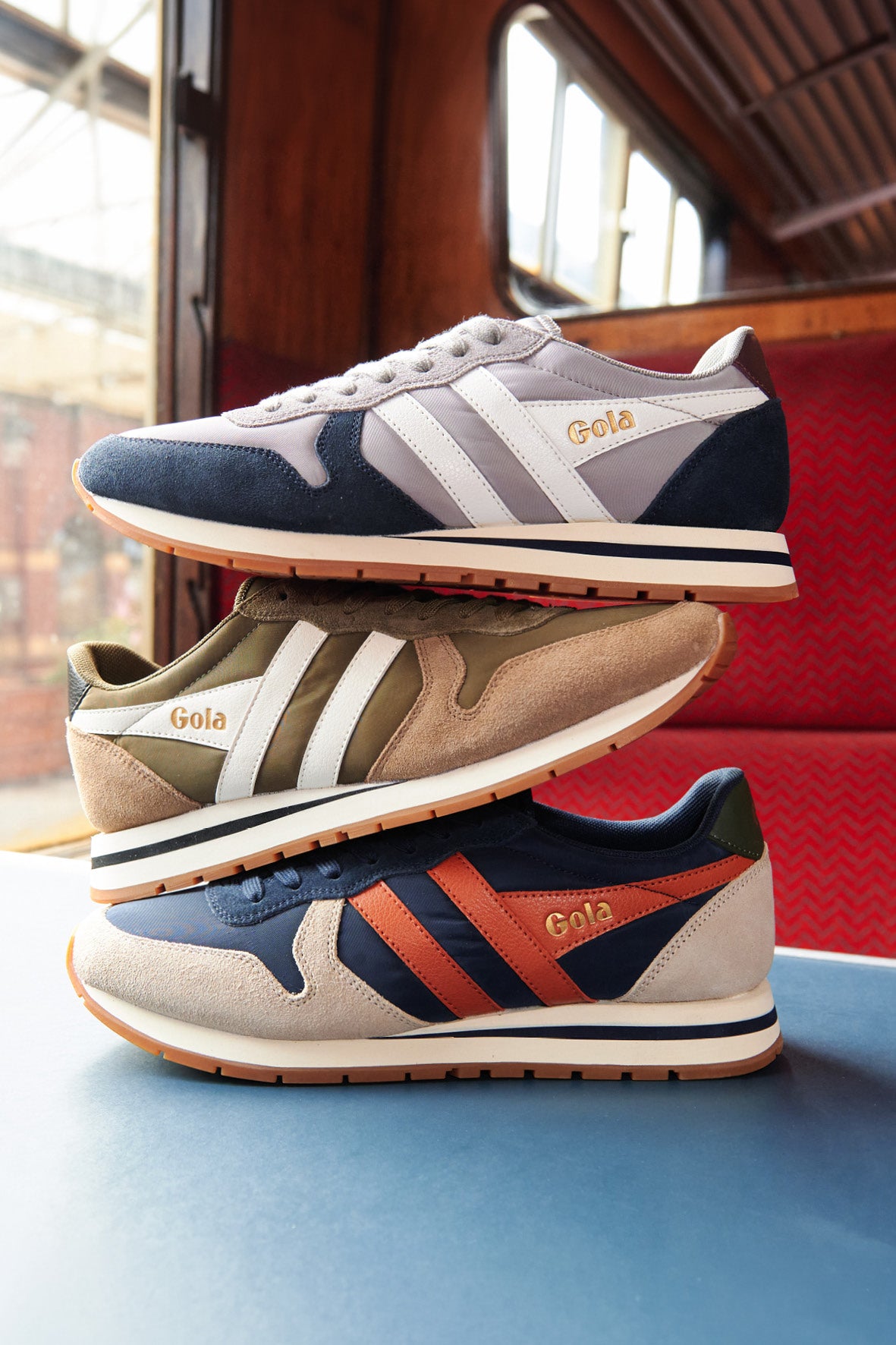 Three pairs of Gola trainers stacked, in navy/grey, khaki/beige, and navy/orange