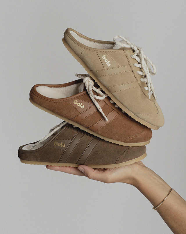 Three stacked Gola suede mule trainers in beige brown and dark brown held in a hand