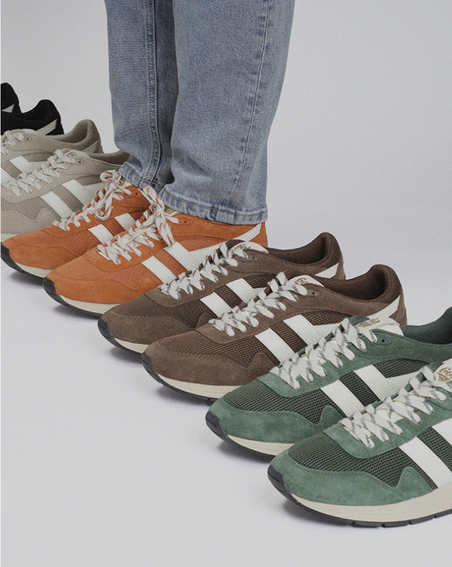 Person wearing blue jeans standing in a row of multi-coloured suede and mesh trainers