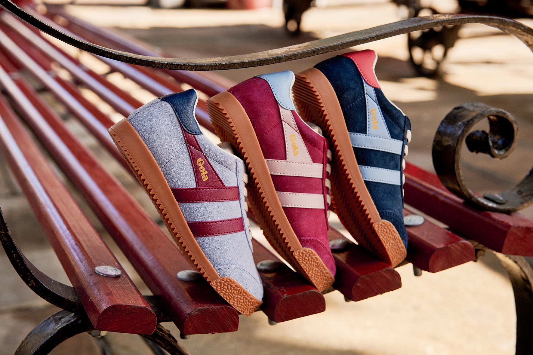 Four colorful sneakers with brown soles lined up on a wooden park bench.