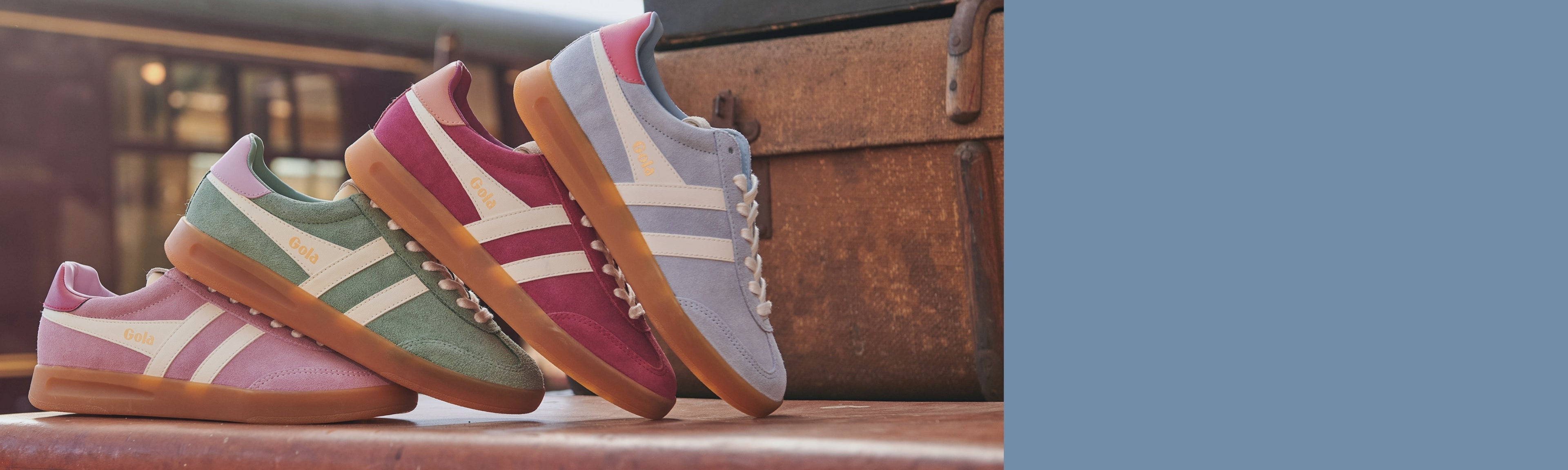 Three Gola trainers in pink, green, and blue, with white stripes and gum soles, on a wooden surface