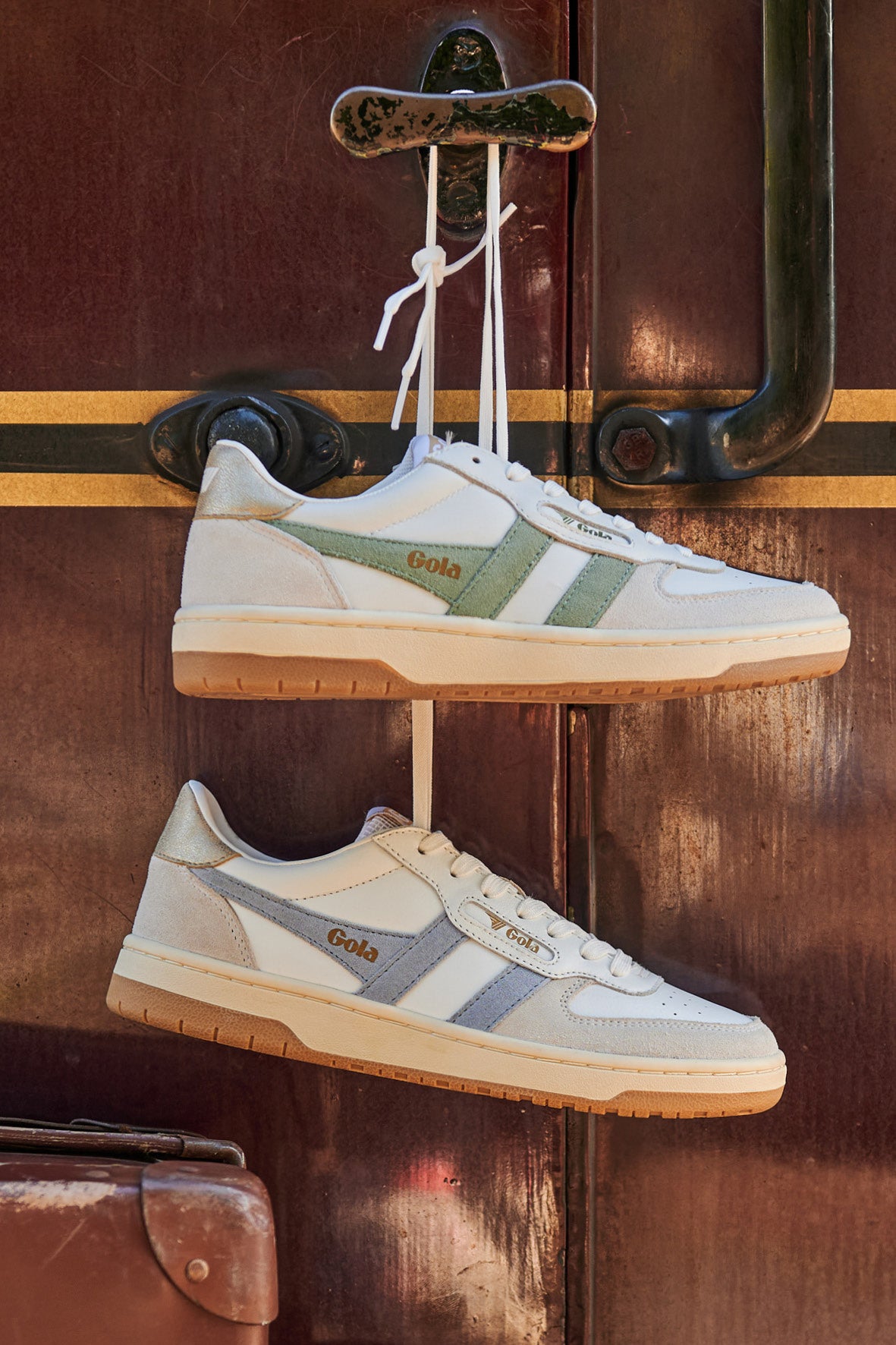 Two pairs of Gola trainers hanging from a door handle, one with green stripes, one with blue stripes