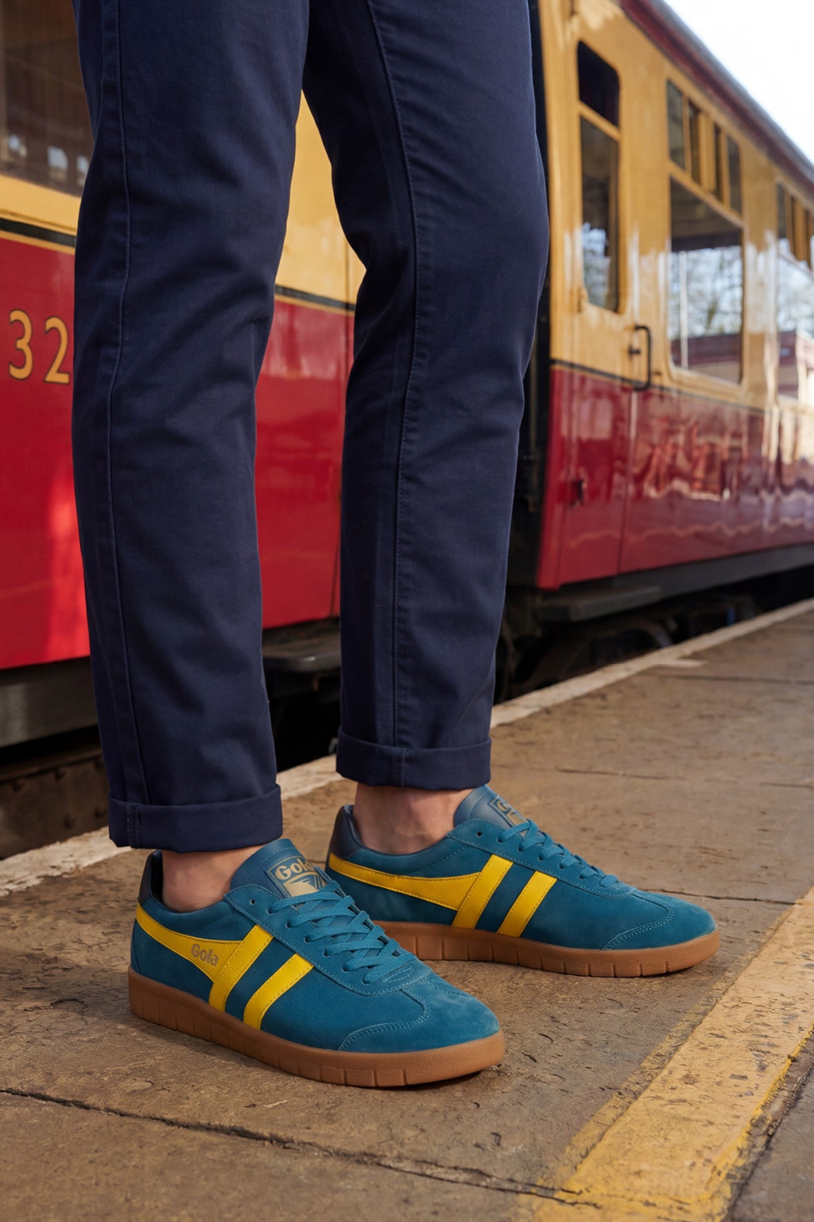 Person wearing blue Gola trainers with yellow stripes and blue trousers on a train platform