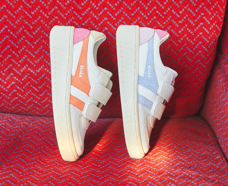 Two Gola sneakers, one with pink and orange accents, the other with pink and blue, on a red patterned surface.