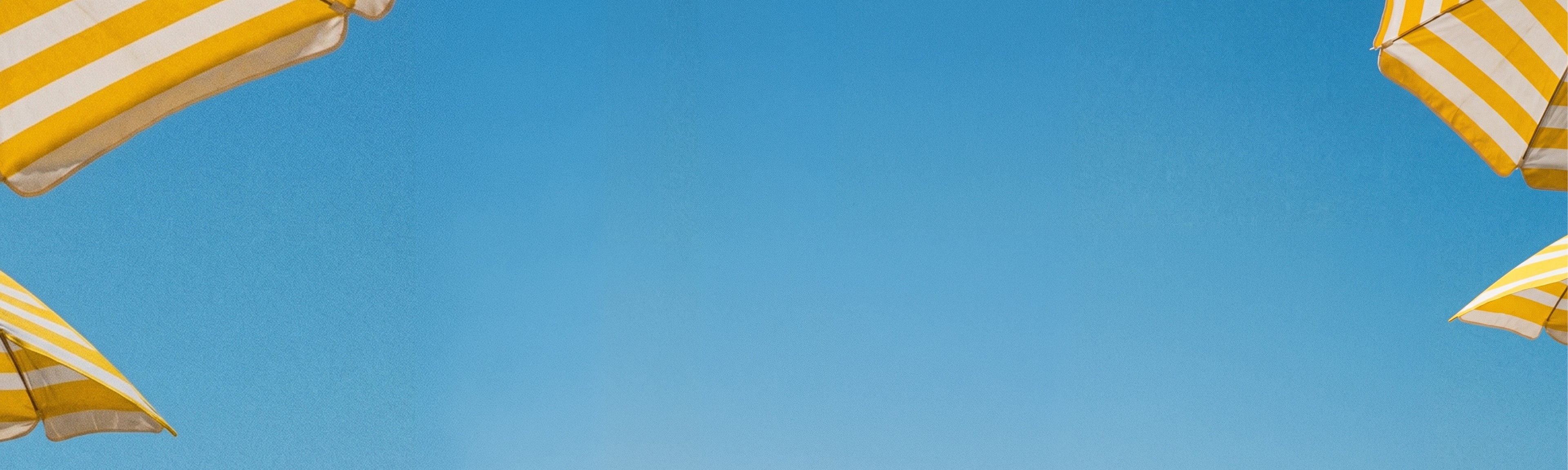 Yellow and white striped beach umbrellas against a clear blue sky