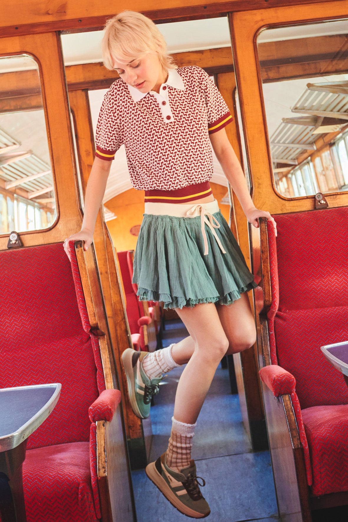Woman in a red and white patterned polo shirt and green skirt, standing in a train carriage