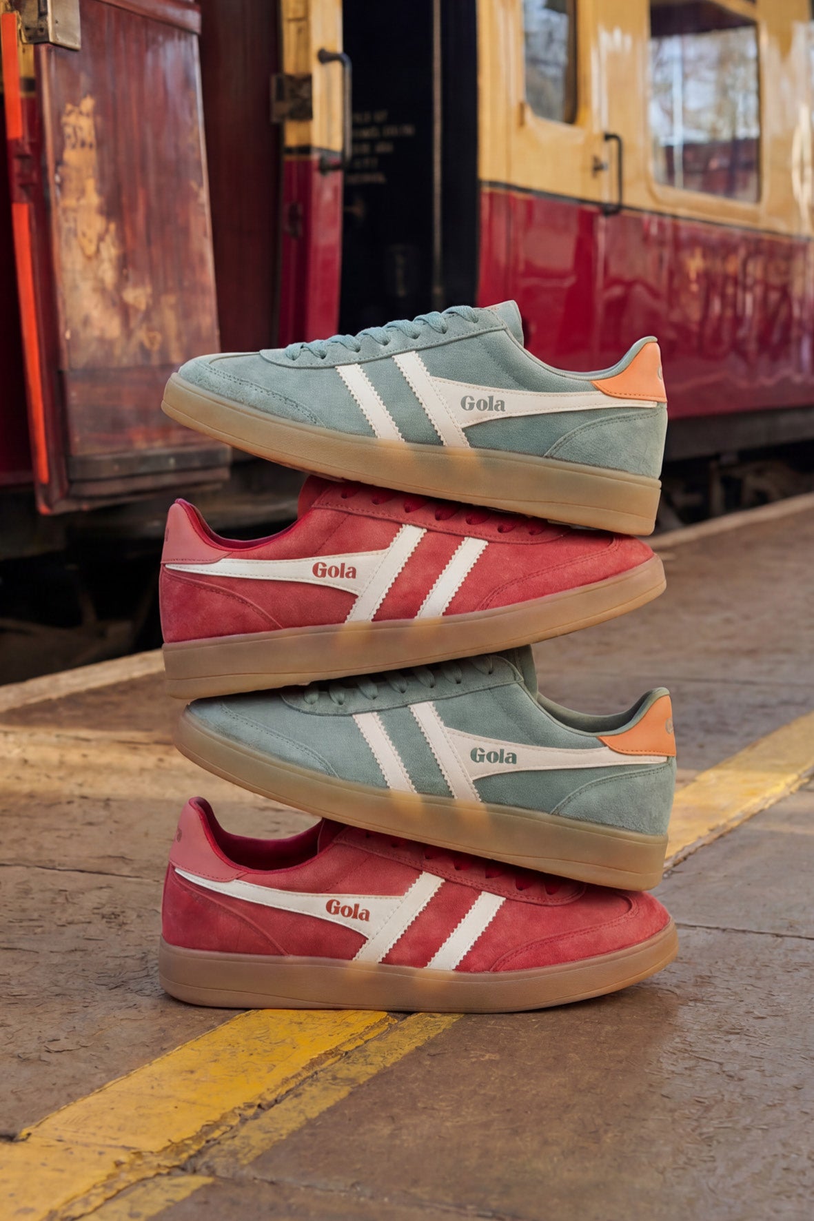Four Gola trainers stacked on a platform, two blue and two red, with a train in the background