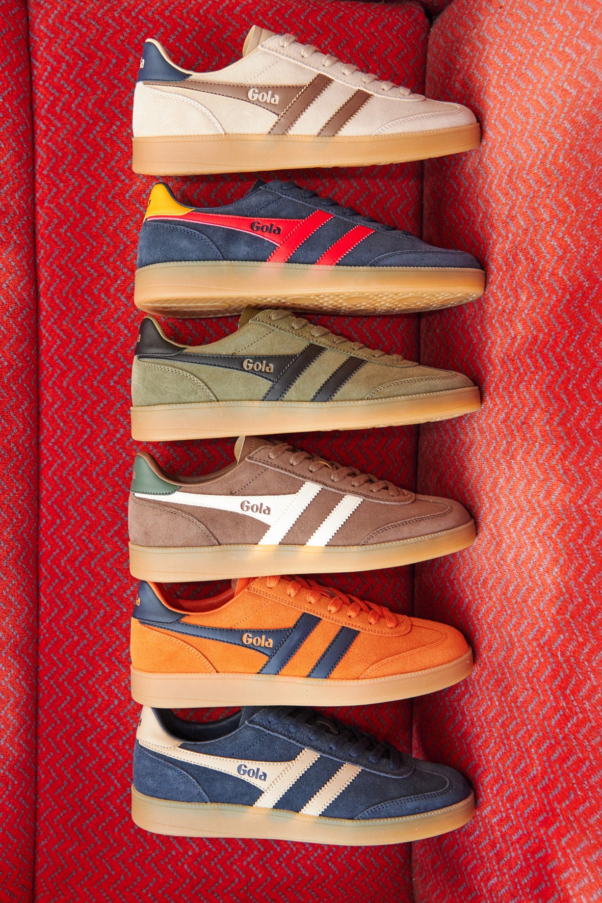 Six pairs of Gola trainers in various colours, arranged vertically on a red textured surface